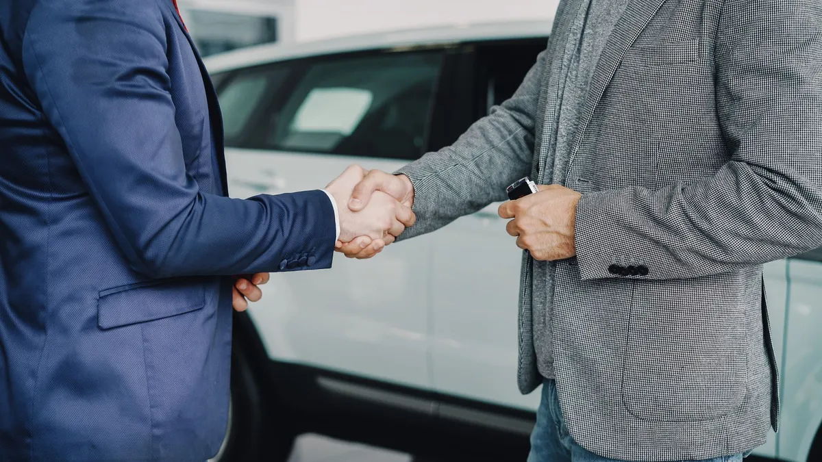 Two people shaking hands in front of a car, exchanging keys
