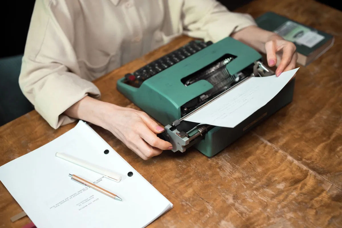 A person feeding paper into a vintage typewriter at a wooden desk