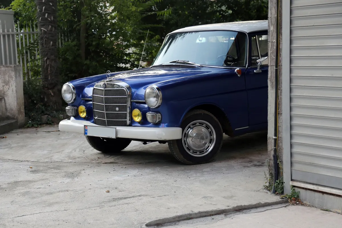 A restored classic blue sedan parked outside a garage