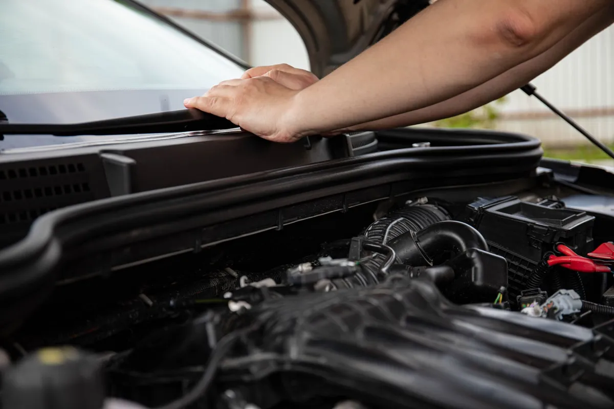 A hand resting on the open hood of a car during an inspection of the engine bay