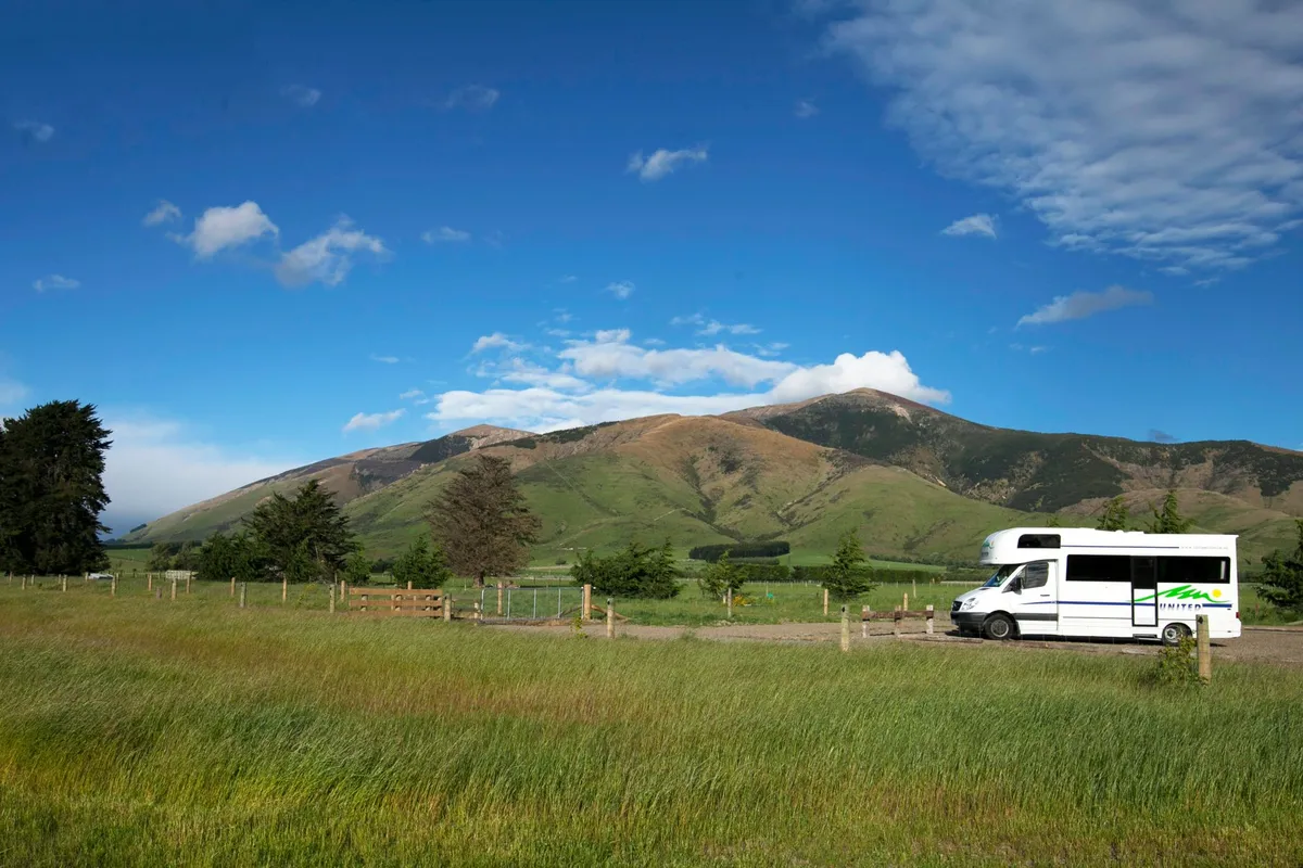 A motorhome parked in an open grassy field with mountains in the background