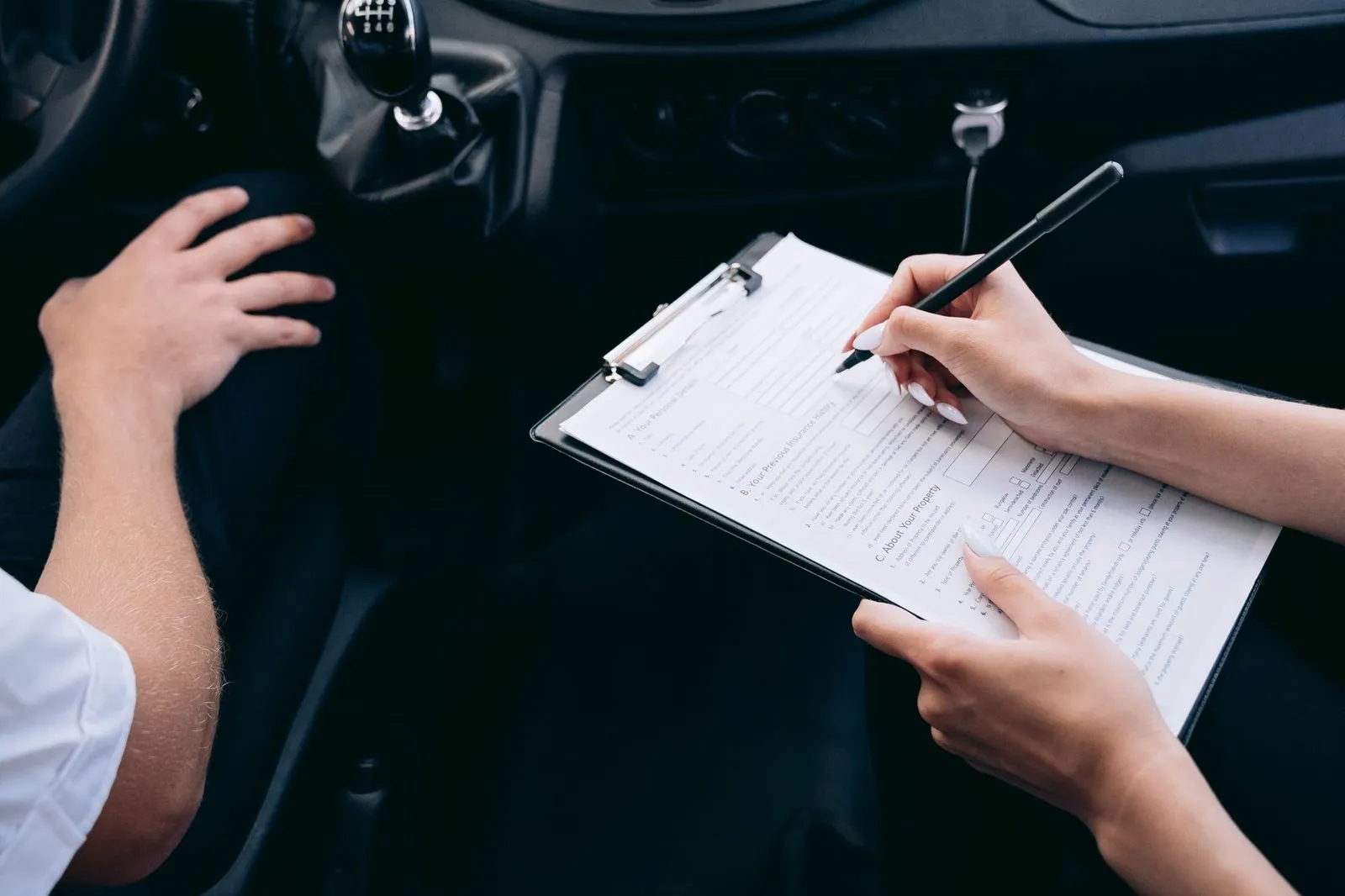 An insurance form on a clipboard being filled out inside a vehicle