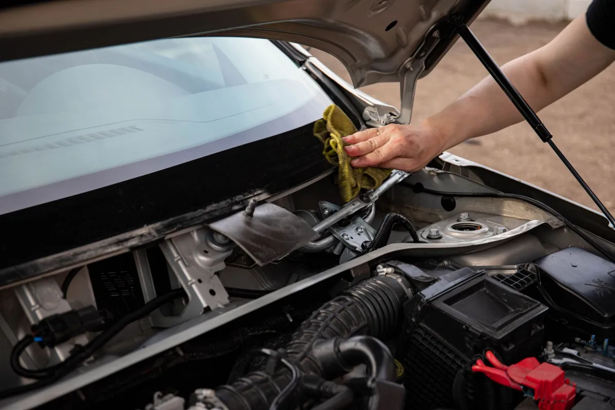 A hand wiping the windshield cowl area of a car with the hood open